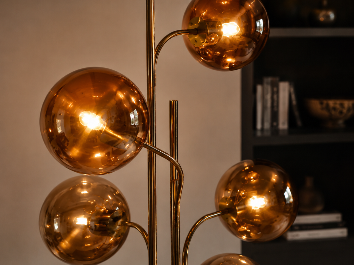 Cluster floor lamp with five amber globe heads on a gold stem beside a sofa in a warm living room