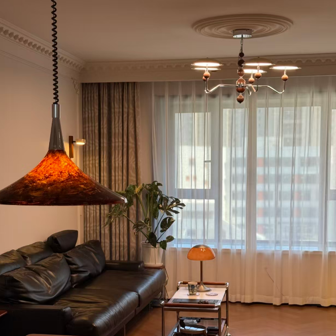 Modern living room with a chandelier, pendant light, and large window.