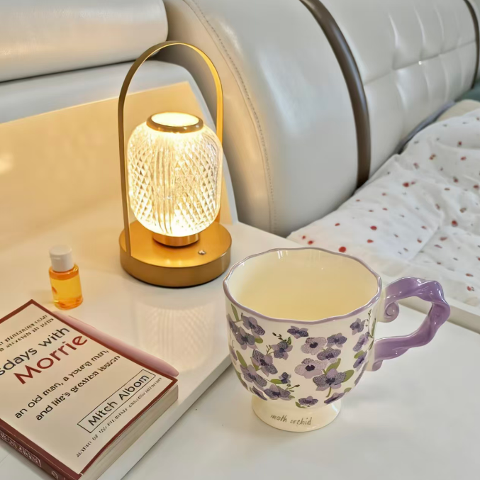 Mug with floral design on a table next to a small lamp and book