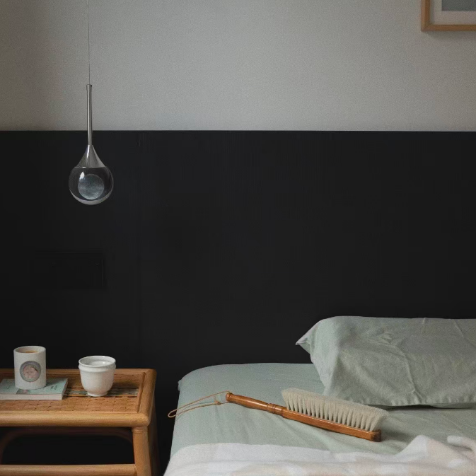 Bedroom with a dark headboard, bedside table with a candle, and a hanging light fixture.