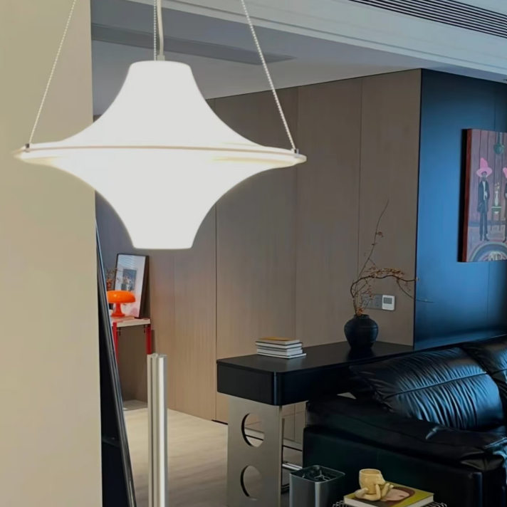 A modern pendant light with a white starburst-shaped shade and thin gold-toned metal accents, hanging in a contemporary living room setting.