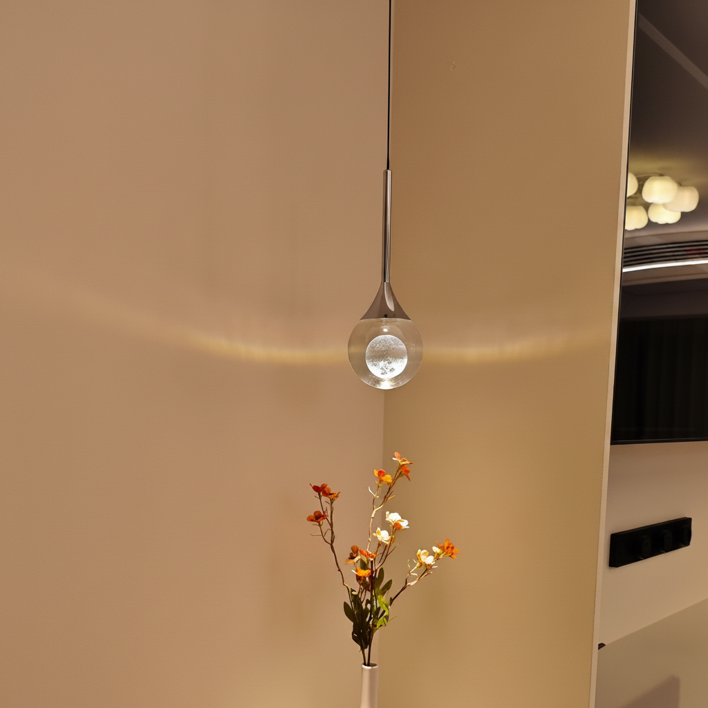 Modern pendant light fixture hanging above a white vase with flowers on a shelf.