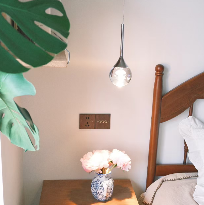 Vase with flowers on a wooden nightstand next to a bed with a wooden headboard.