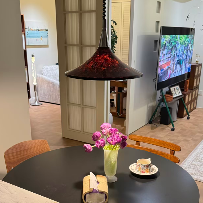 Dining table with a vase of pink flowers, a roll of paper, and a cup in a modern living room.