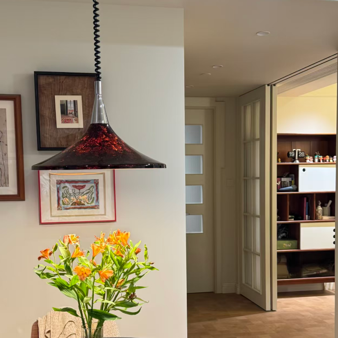 Vase with flowers and an apple on a table in a room with a bookshelf and framed pictures.
